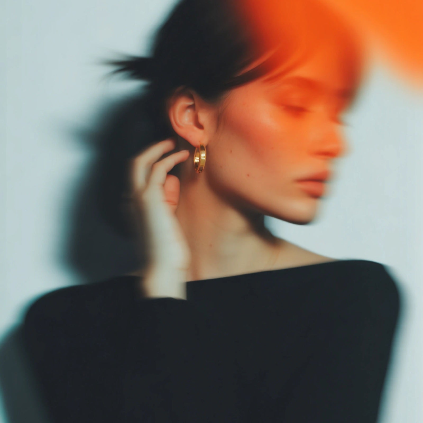 A solid gold hoop earring worn with hair tied back